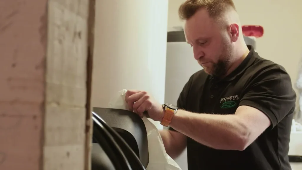 Kadr z filmu EcoWater: technik rozpakowuje zmiękczacz wody przed montażem